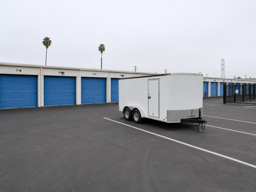 Trailer in a parking lot of Low Cost Storage Self Storage, Paramount, CA, with blue roll-up doors and palm trees in view.